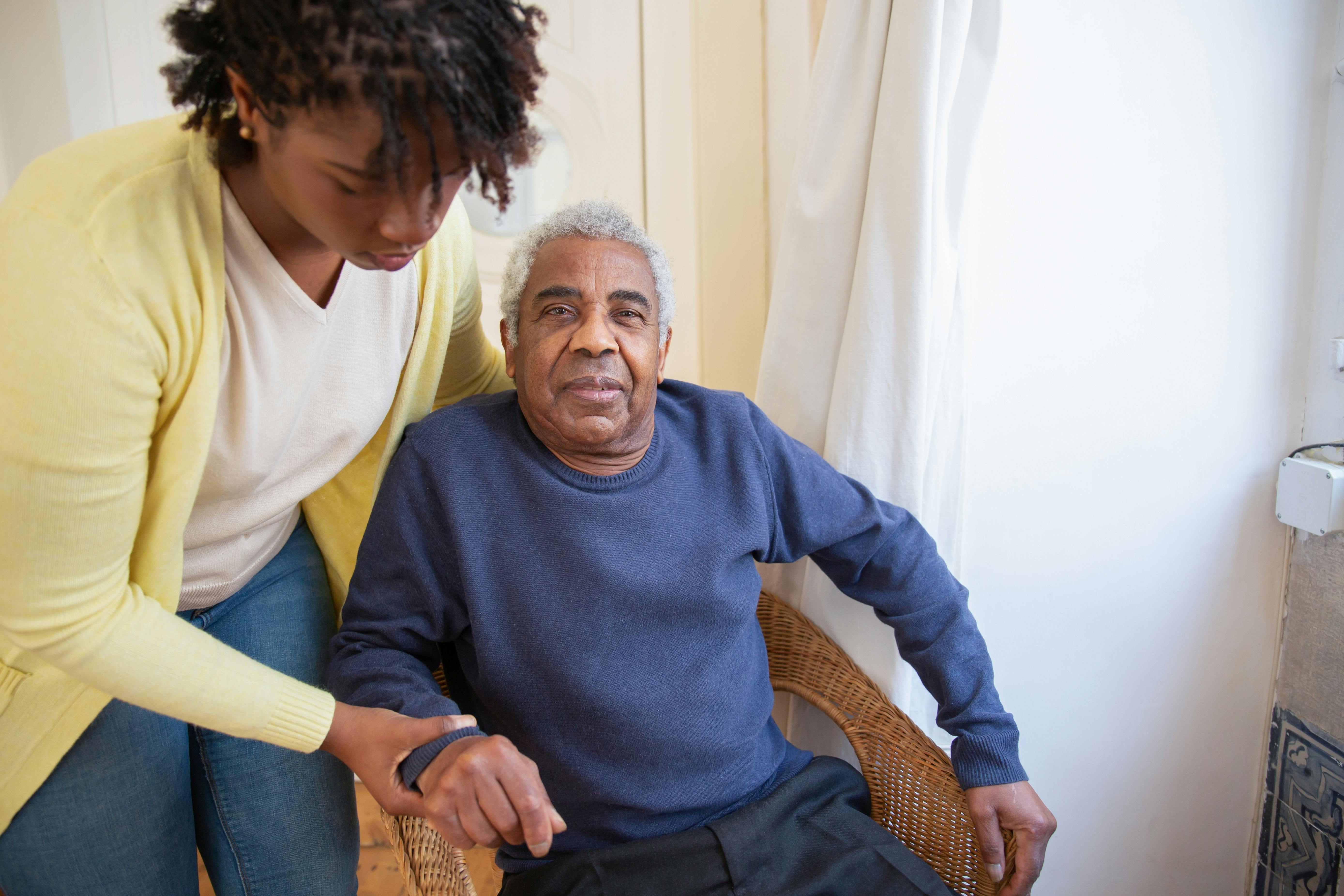 A woman assists an elderly man indoors, focusing on care and support